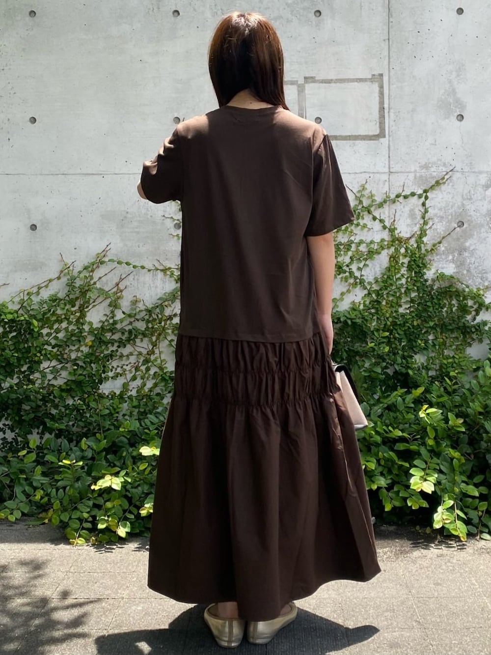 ブラウン系のワンピース、ブラック系のショルダーバッグ、ゴールド系のパンプスを着用したレディースの夏コーディネートの2枚目の写真