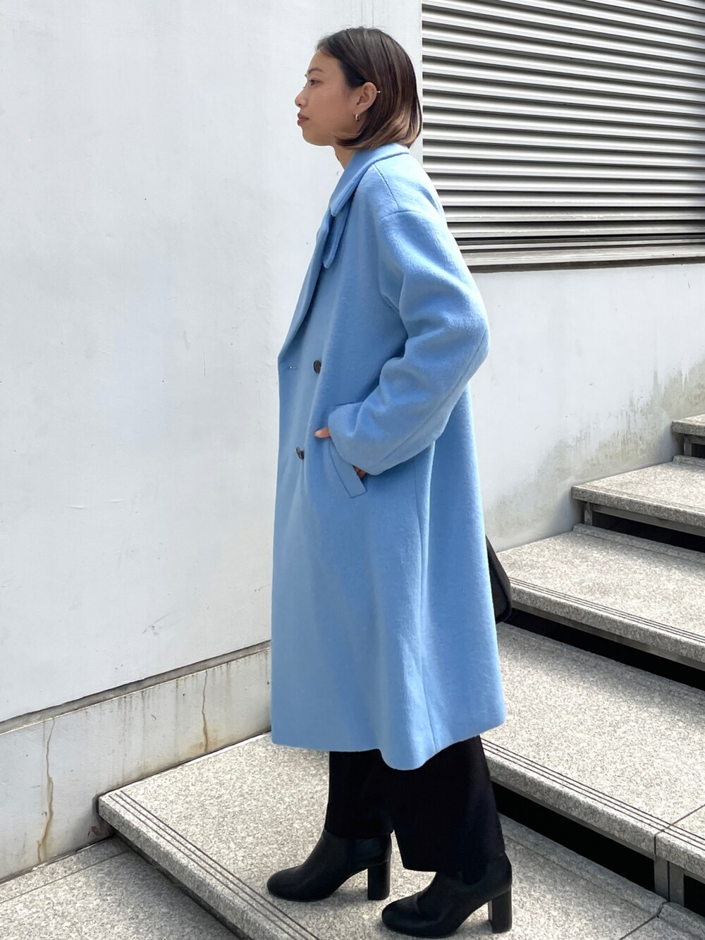 ブルー系のチェスターコート、ホワイト系のニット/セーター、ブラック系のその他パンツを着用したレディースの冬コーディネートの2枚目の写真