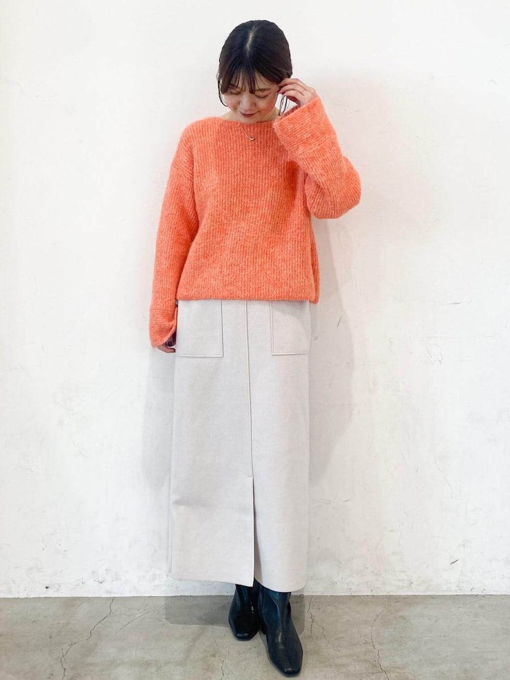 ブラック系のチェスターコート、オレンジ系のニット/セーター、ベージュ系のスカートを着用したレディースの冬コーディネートの5枚目の写真