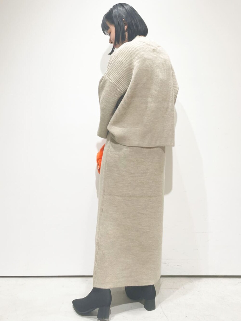 ベージュ系のニット/セーター、ベージュ系のスカート、ブラック系のブーツを着用したレディースの秋コーディネートの2枚目の写真