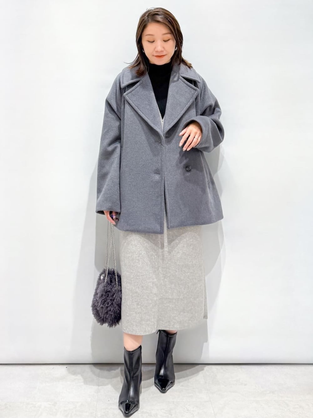 ブラック系のニット/セーター、グレー系のピーコート、グレー系のショルダーバッグを着用したレディースの秋コーディネートの2枚目の写真