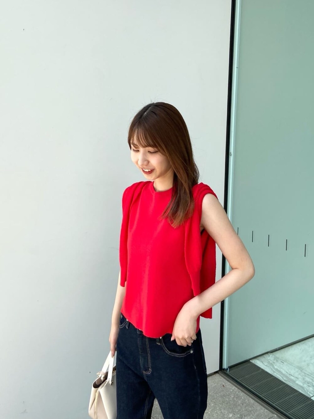 レッド系のカーディガン/ボレロ、レッド系のニット/セーター、ブルー系のデニムパンツを着用したレディースの夏コーディネートの6枚目の写真