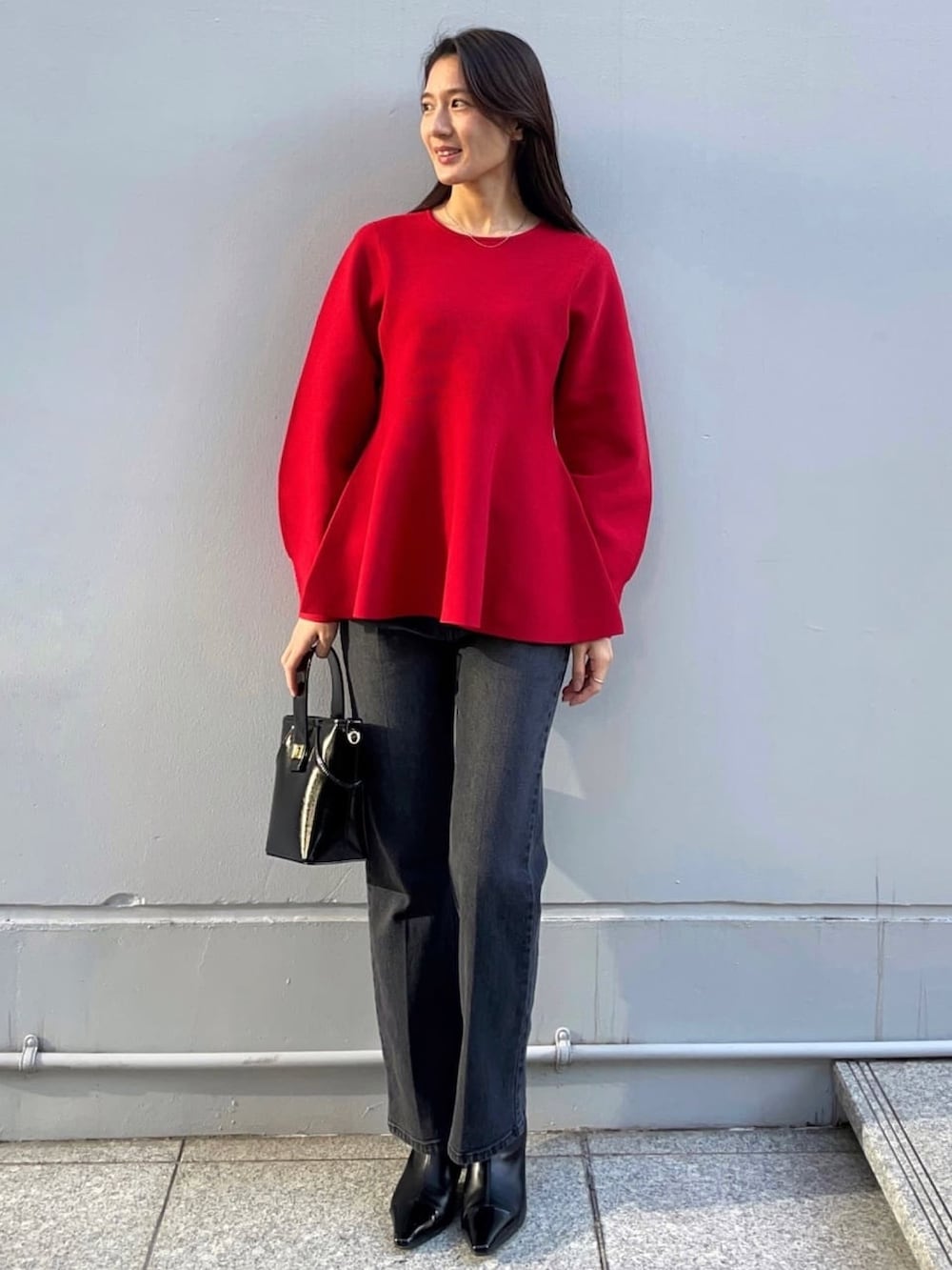 レッド系のニット/セーター、ブラック系のノーカラーコート、ブラック系のデニムパンツを着用したレディースの冬コーディネートの5枚目の写真