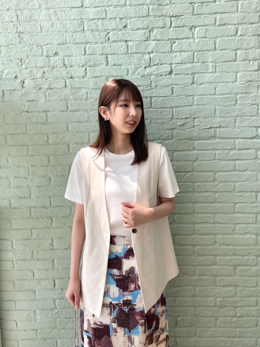 ベージュ系のベスト、ホワイト系のTシャツ/カットソー、レッド系のスカートを着用したレディースの夏コーディネートの6枚目の写真