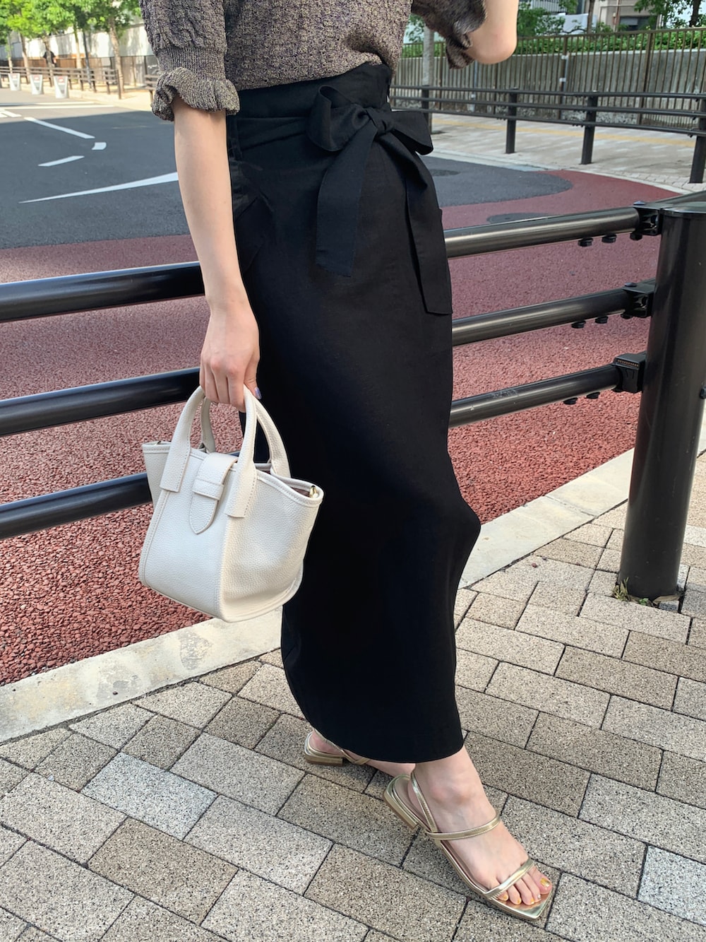 パープル系のニット/セーター、ブラック系のスカート、ゴールド系のサンダルを着用したレディースの夏コーディネートの4枚目の写真