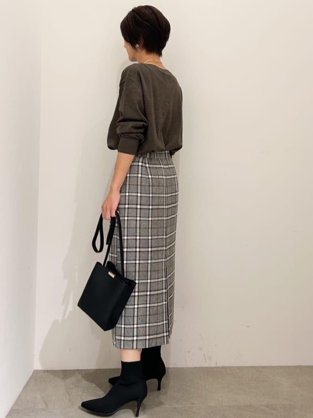 ブラック系のスカート、ブラック系のショルダーバッグ、ブラック系のブーツを着用したレディースの秋コーディネートの2枚目の写真