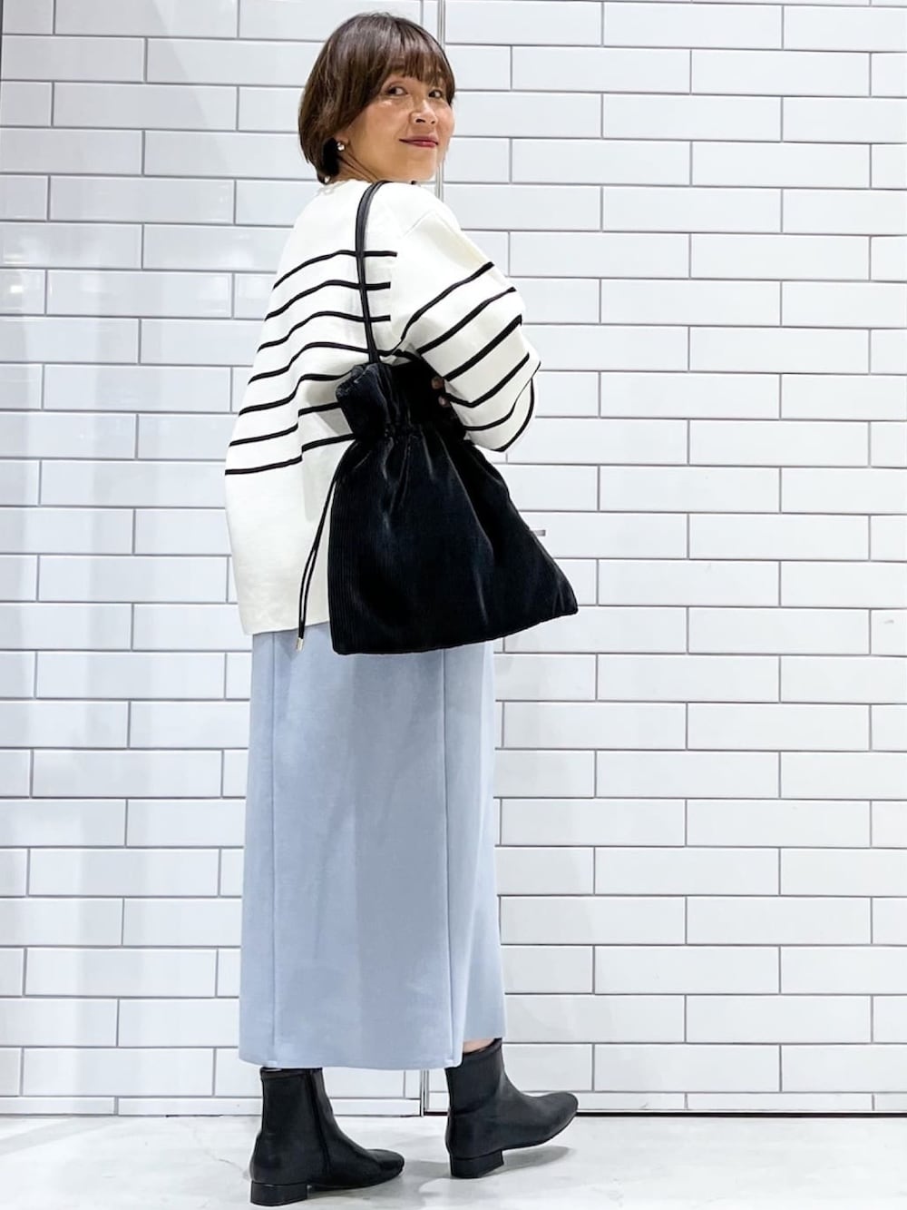 ホワイト系のニット/セーター、ブルー系のスカート、ブラック系のトートバッグを着用したレディースの冬コーディネートの2枚目の写真