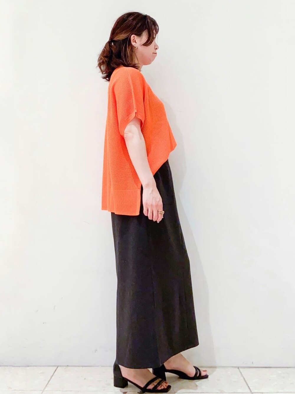 オレンジ系のニット/セーター、グレー系のスカート、ブラック系のショルダーバッグを着用したレディースの夏コーディネートの2枚目の写真