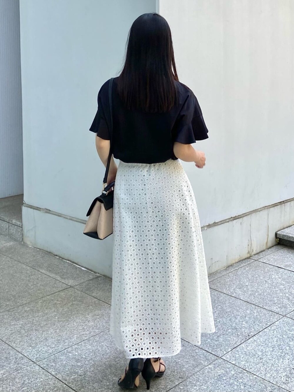 ブラック系のTシャツ/カットソー、ホワイト系のスカート、ブラック系のサンダルを着用したレディースの春コーディネートの3枚目の写真