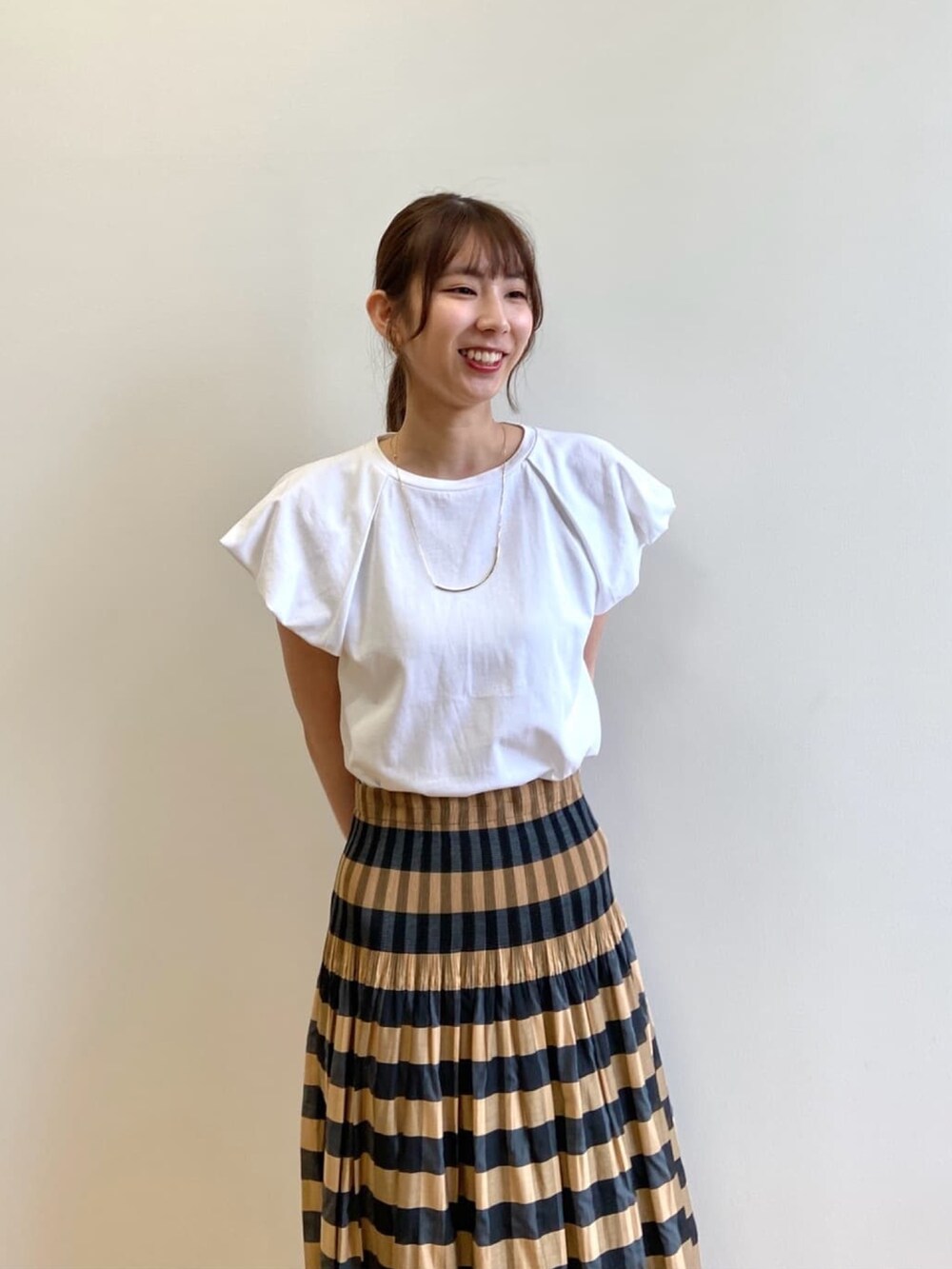 ベージュ系のスカート、ホワイト系のTシャツ/カットソー、ブラック系のサンダルを着用したレディースの夏コーディネートの5枚目の写真