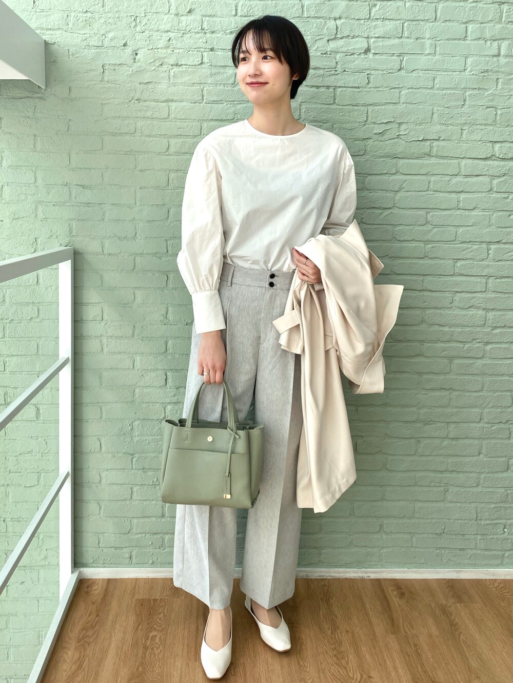 グリーン系のトートバッグ、ホワイト系のシャツ/ブラウス、ホワイト系のトレンチコートを着用したレディースの春コーディネートの2枚目の写真