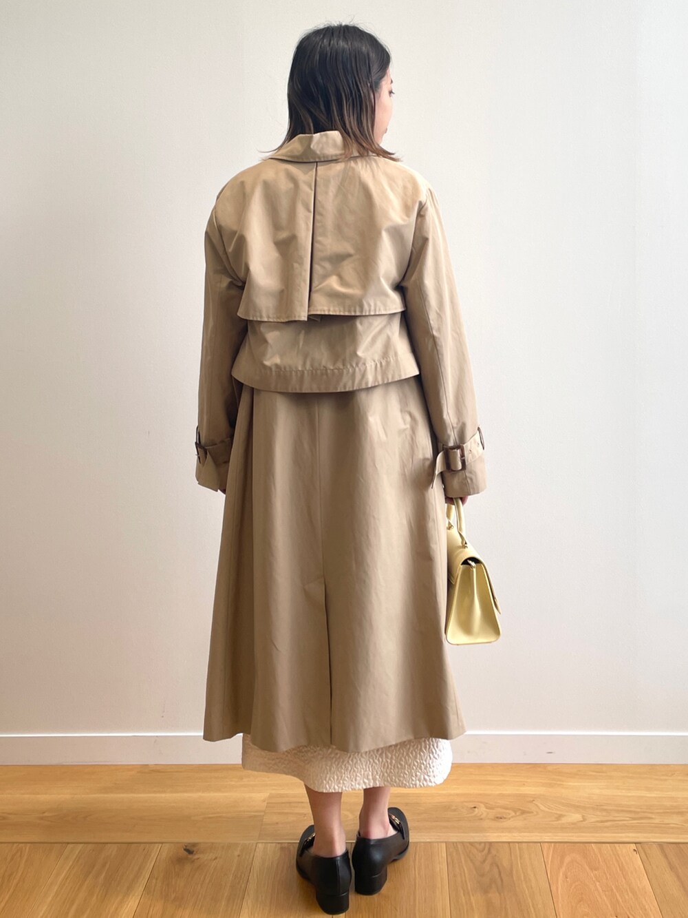 ベージュ系のトレンチコート、ホワイト系のワンピース、イエロー系のショルダーバッグを着用したレディースの春コーディネートの3枚目の写真