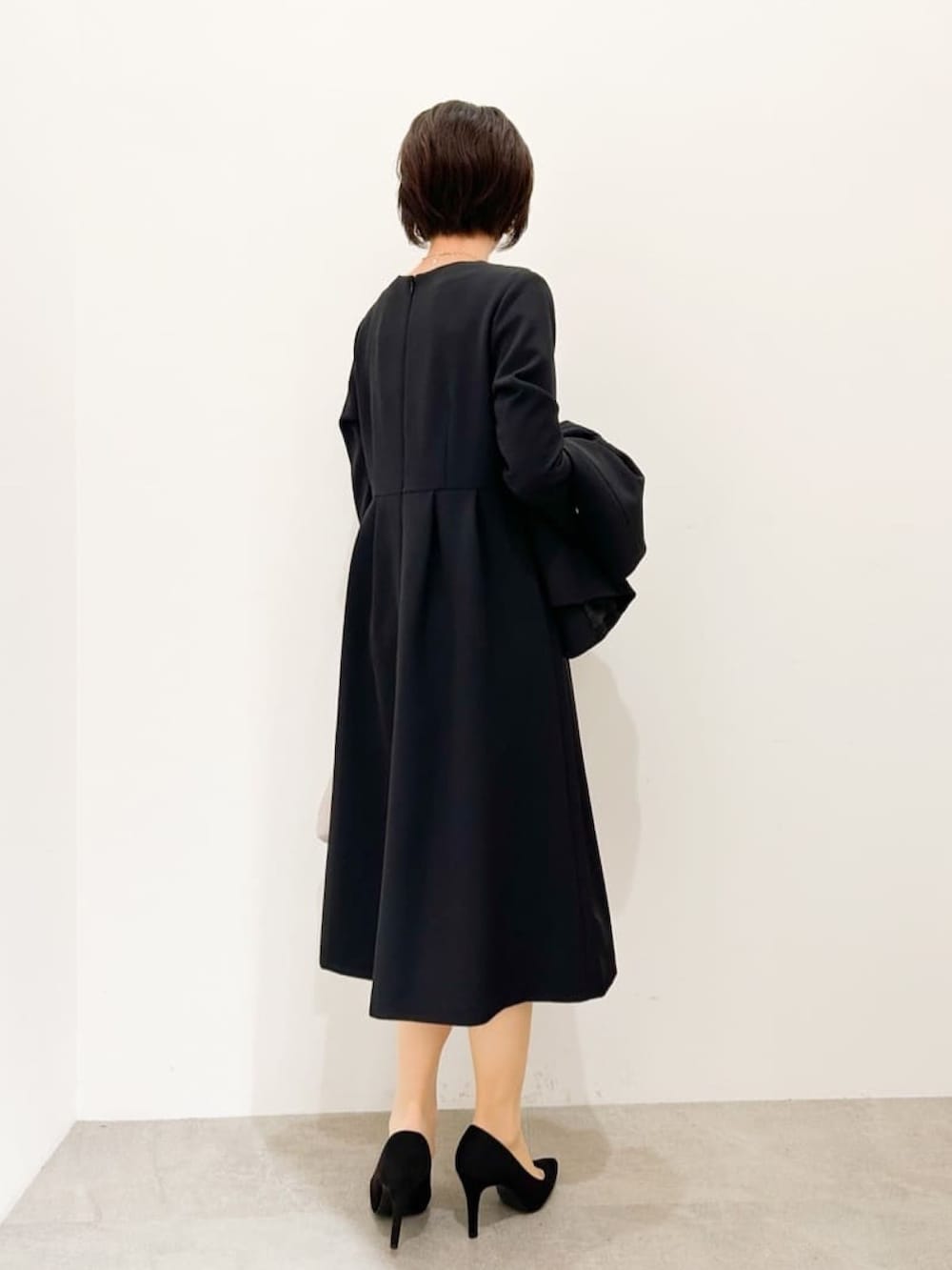 ブラック系のパンプス、ブラック系のワンピース、グレー系のショルダーバッグを着用したレディースの冬コーディネートの2枚目の写真