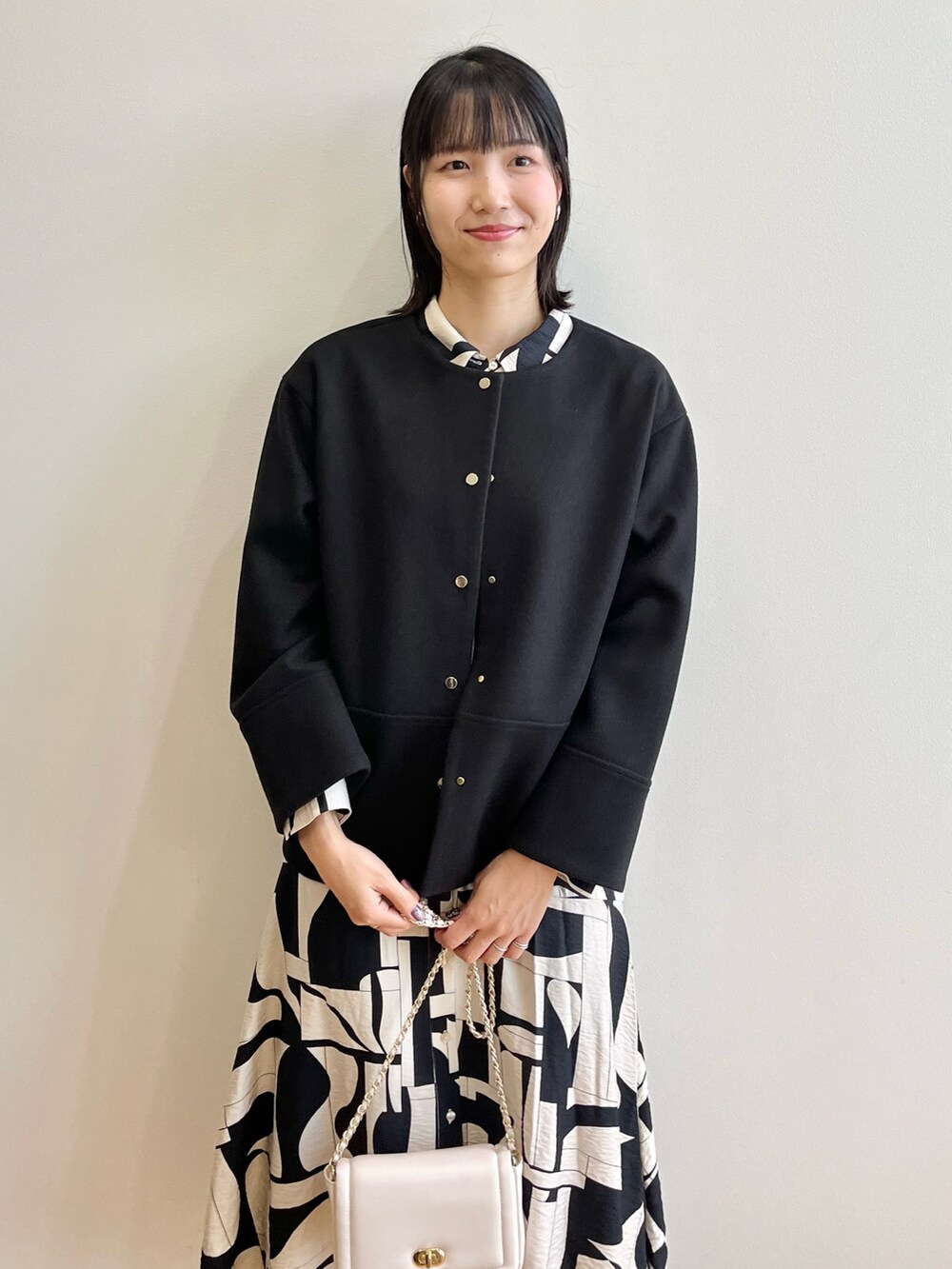 ブラック系のノーカラーコート、ベージュ系のワンピース、ブラック系のブーツを着用したレディースの秋コーディネートの6枚目の写真