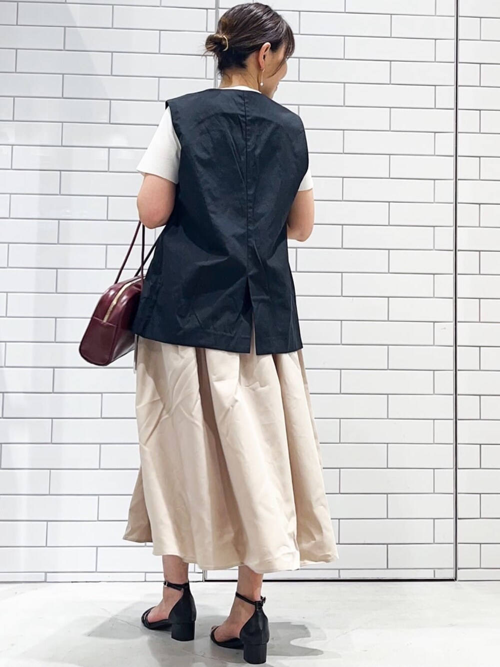 ブラック系のベスト、ベージュ系のワンピース、ブラック系のサンダルを着用したレディースの夏コーディネートの2枚目の写真