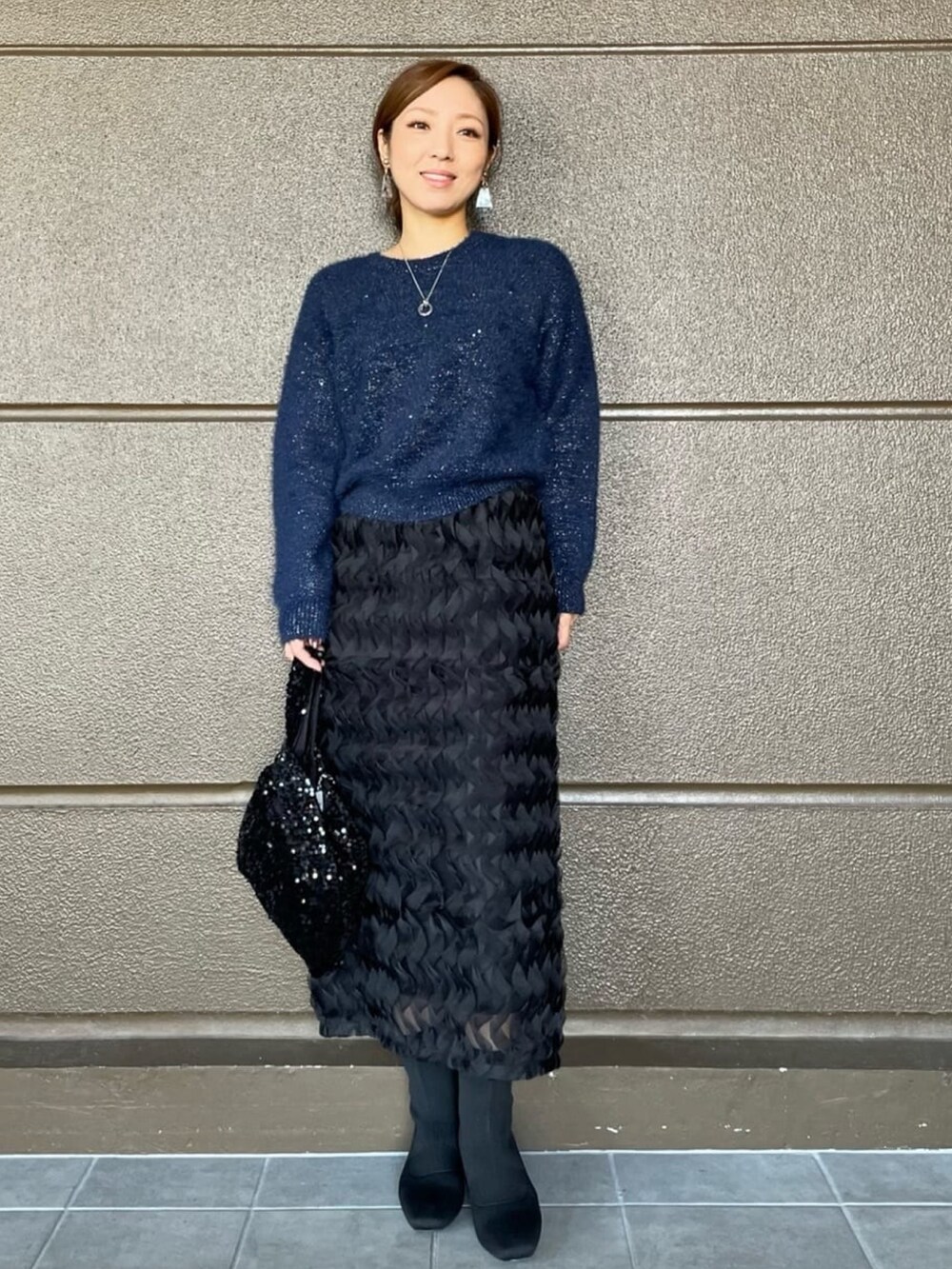 ブラック系のスカート、ブルー系のニット/セーター、ブラック系のブーツを着用したレディースの秋コーディネートの2枚目の写真