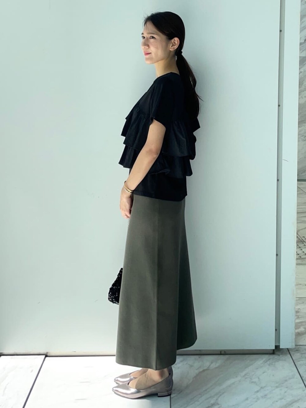 ブラック系のTシャツ/カットソー、グリーン系のスカート、シルバー系のパンプスを着用したレディースの夏コーディネートの3枚目の写真