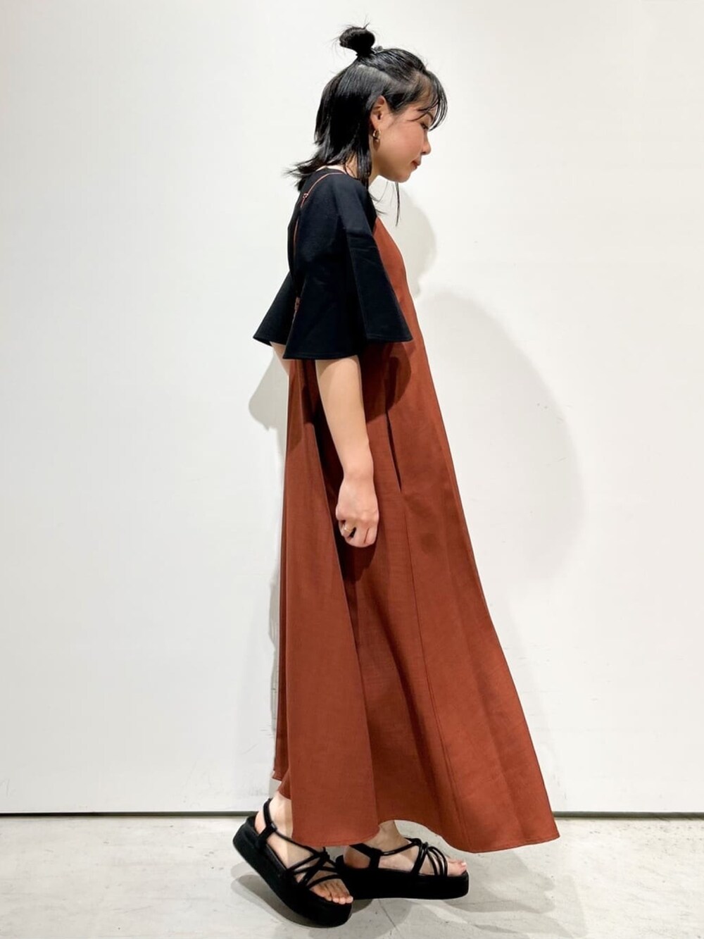 オレンジ系のワンピース、ブラック系のTシャツ/カットソー、ブラック系のサンダルを着用したレディースの夏コーディネートの2枚目の写真