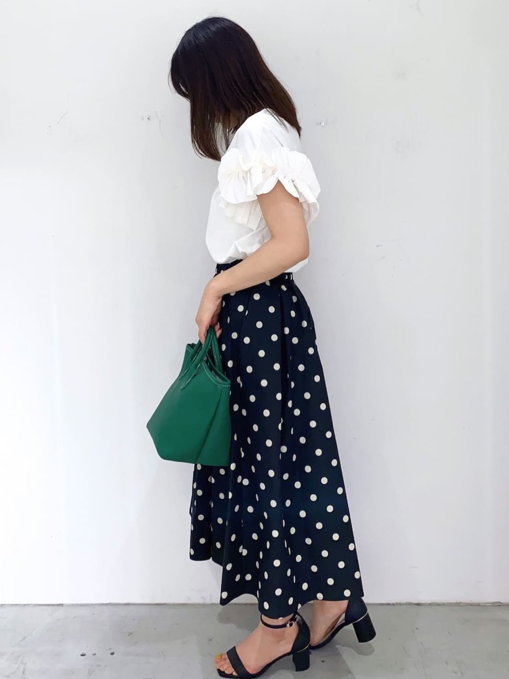グリーン系のトートバッグ、ブラック系のスカート、ホワイト系のTシャツ/カットソーを着用したレディースの秋コーディネートの2枚目の写真