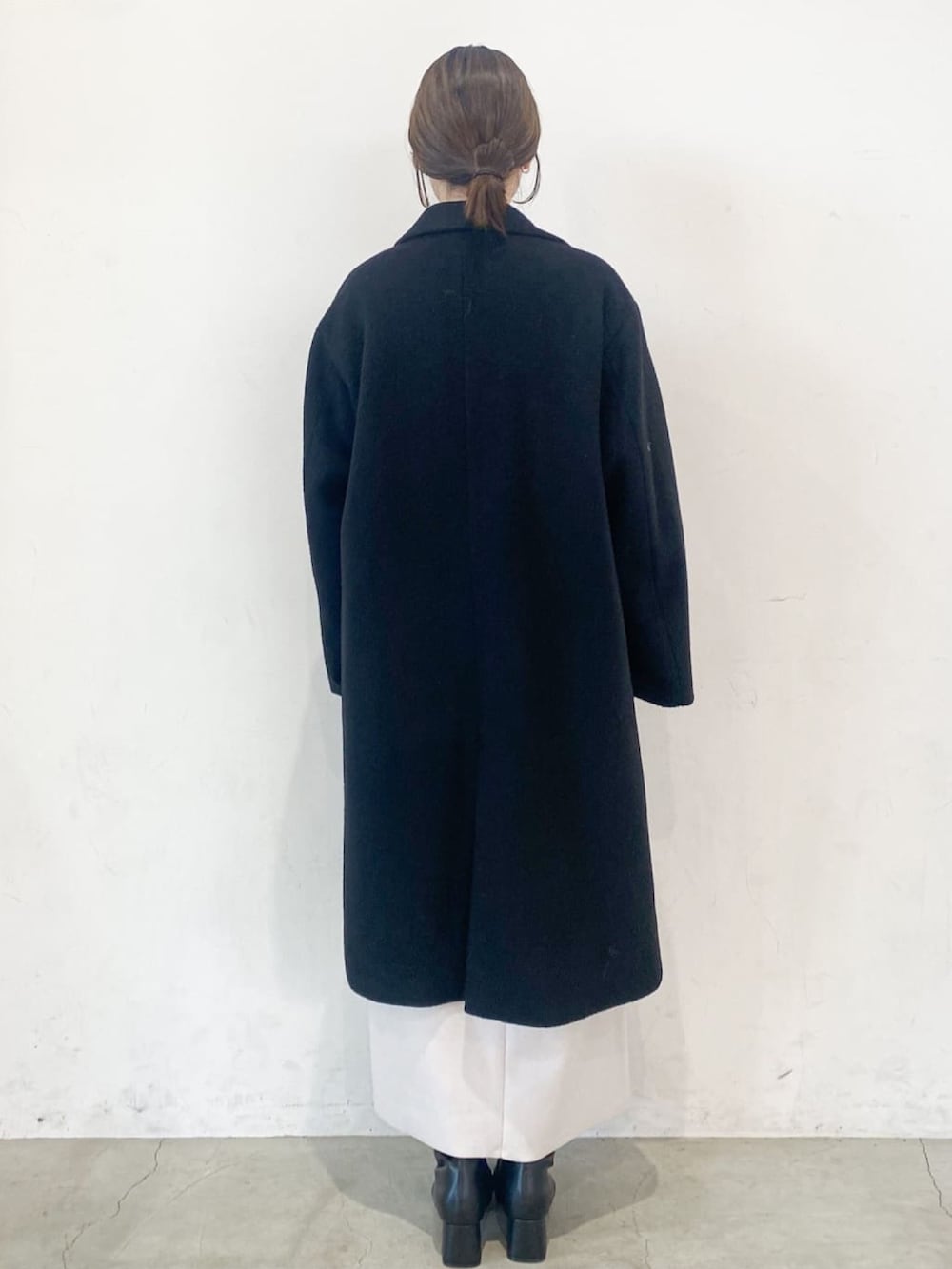 ブラック系のチェスターコート、オレンジ系のニット/セーター、ベージュ系のスカートを着用したレディースの冬コーディネートの4枚目の写真