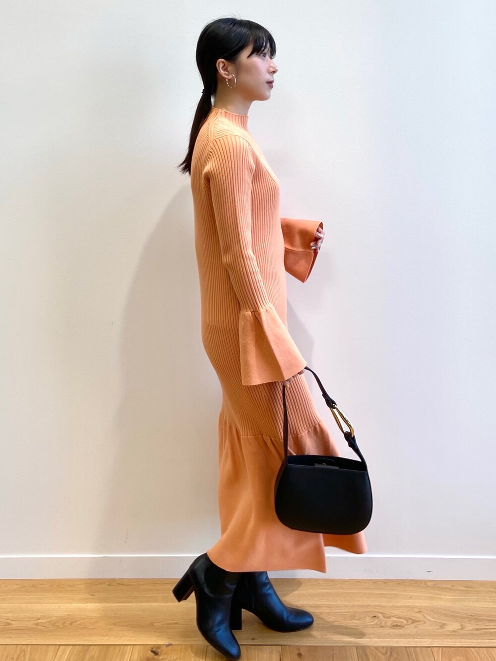 オレンジ系のワンピース、ブラック系のブーツを着用したレディースの冬コーディネートの2枚目の写真