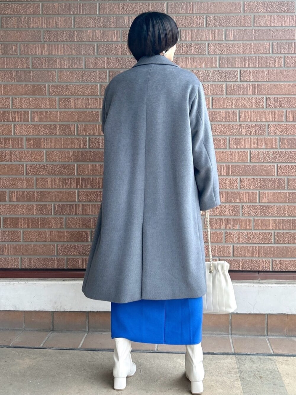 ブルー系のスカート、グレー系のニット/セーター、グレー系のチェスターコートを着用したレディースの秋コーディネートの3枚目の写真