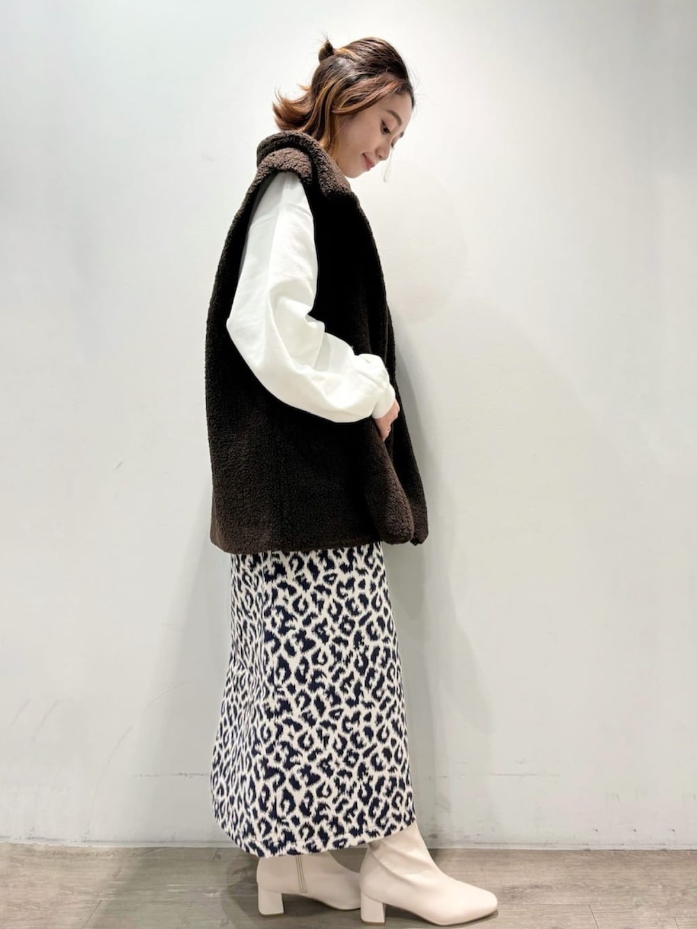 ブルー系のスカート、ブラウン系のベスト、ホワイト系のTシャツ/カットソーを着用したレディースの秋コーディネートの2枚目の写真