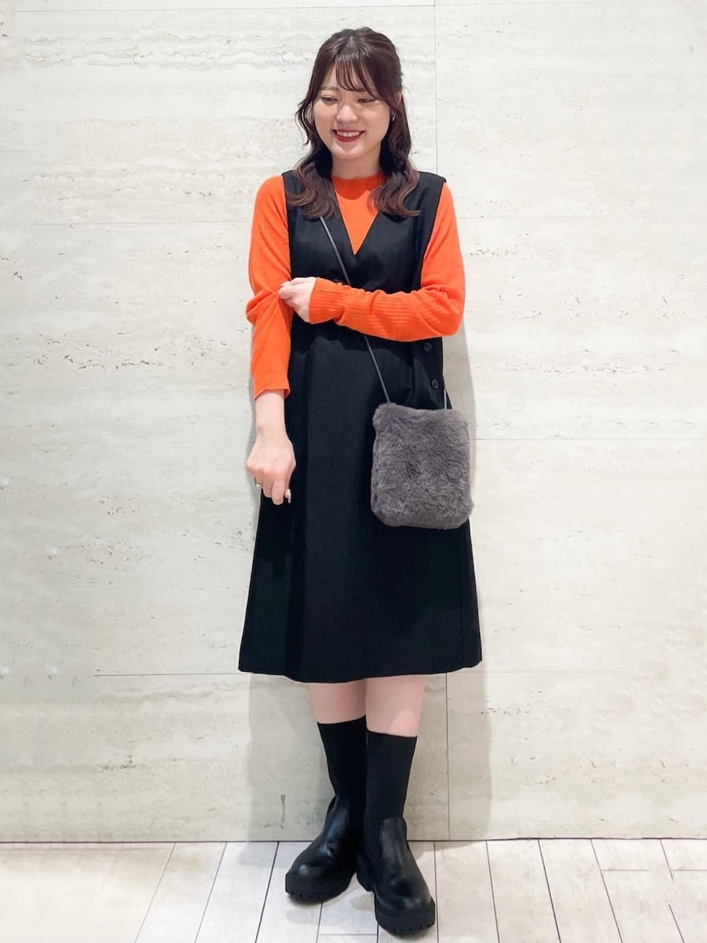 グレー系のノーカラーコート、オレンジ系のニット/セーター、ブラック系のワンピースを着用したレディースの冬コーディネートの3枚目の写真