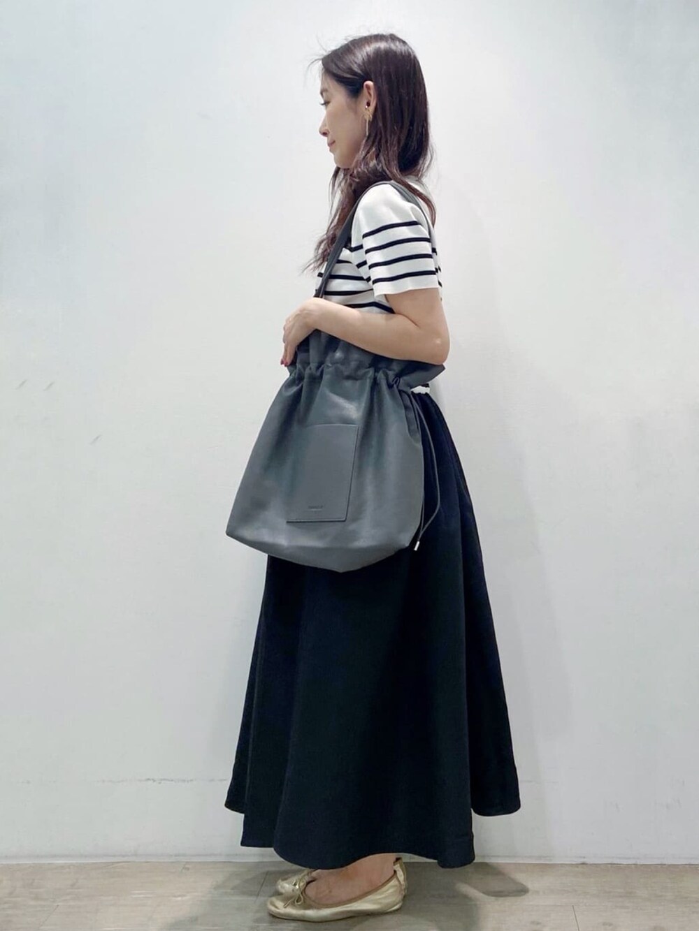 グレー系のトートバッグ、ブラック系のワンピース、ゴールド系のその他シューズを着用したレディースの夏コーディネートの5枚目の写真