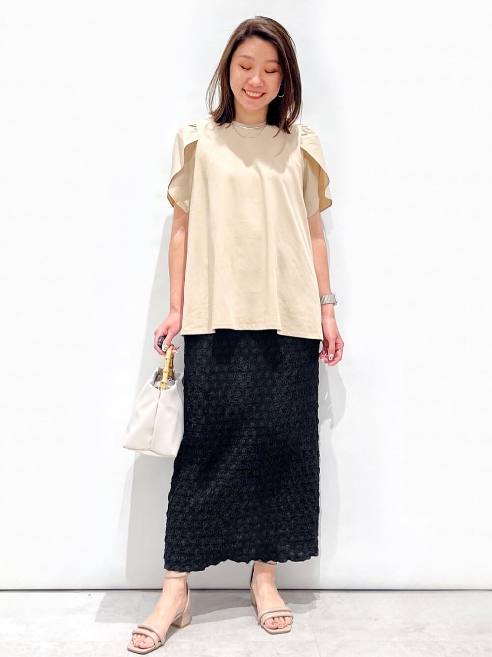 ベージュ系のTシャツ/カットソー、ブラック系のスカート、ホワイト系のショルダーバッグを着用したレディースの春コーディネートの3枚目の写真