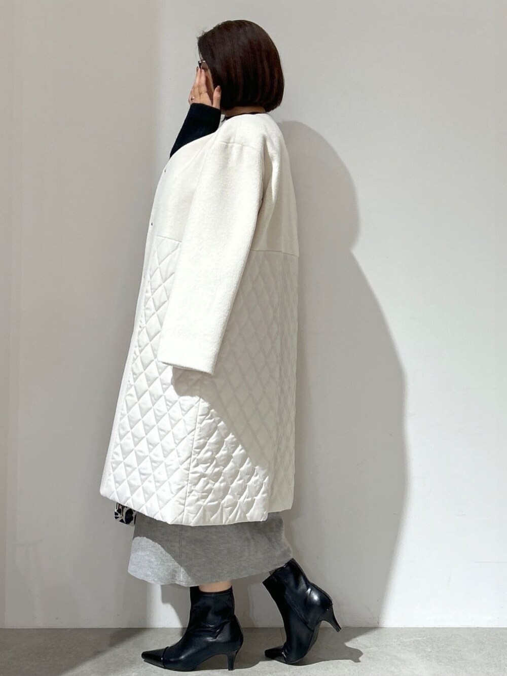 ホワイト系のノーカラーコート、グレー系のスカート、ブラック系のショルダーバッグを着用したレディースの秋コーディネートの3枚目の写真