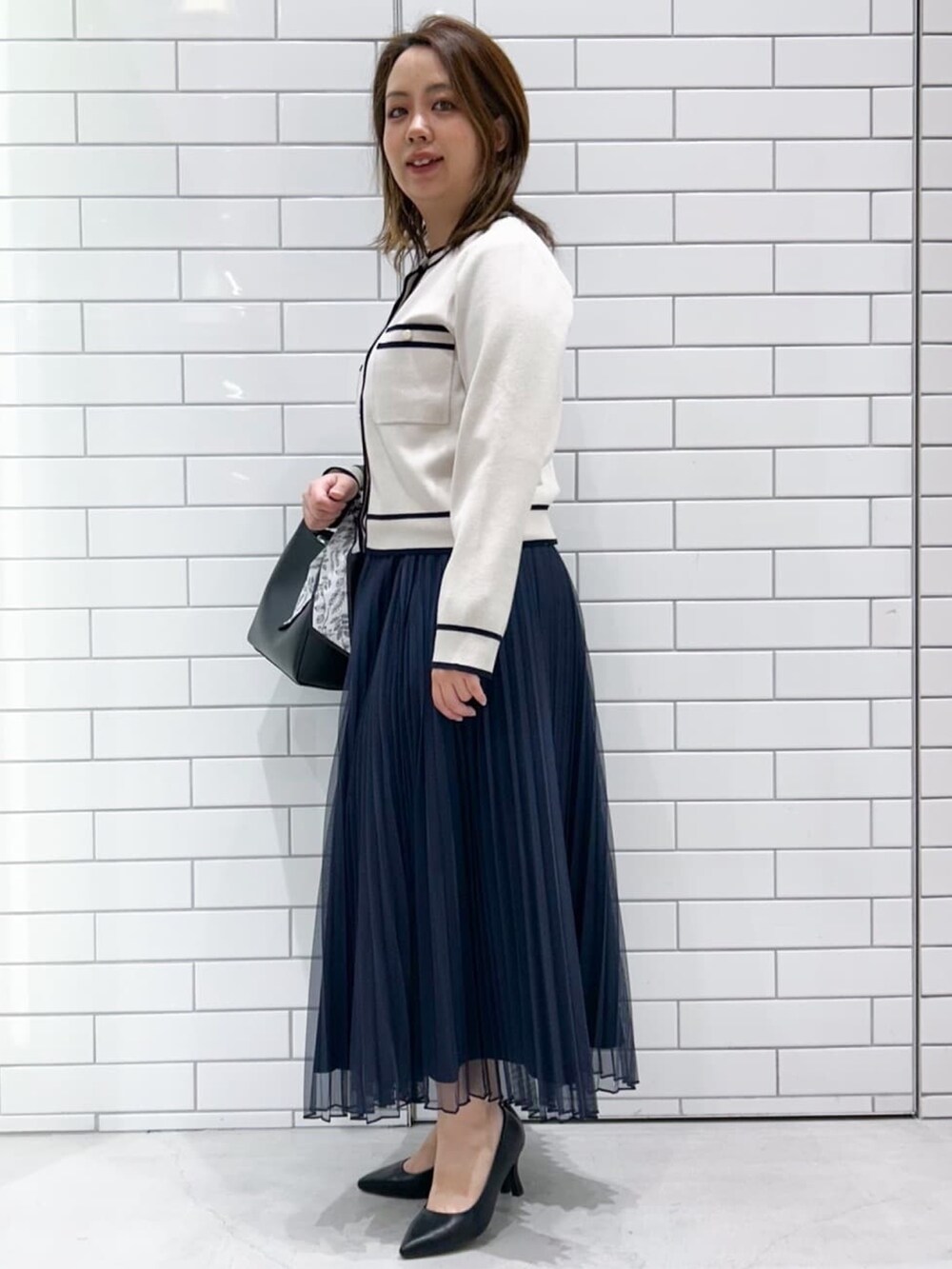 ブルー系のスカート、ホワイト系のカーディガン/ボレロ、ブラック系のトートバッグを着用したレディースの冬コーディネートの2枚目の写真