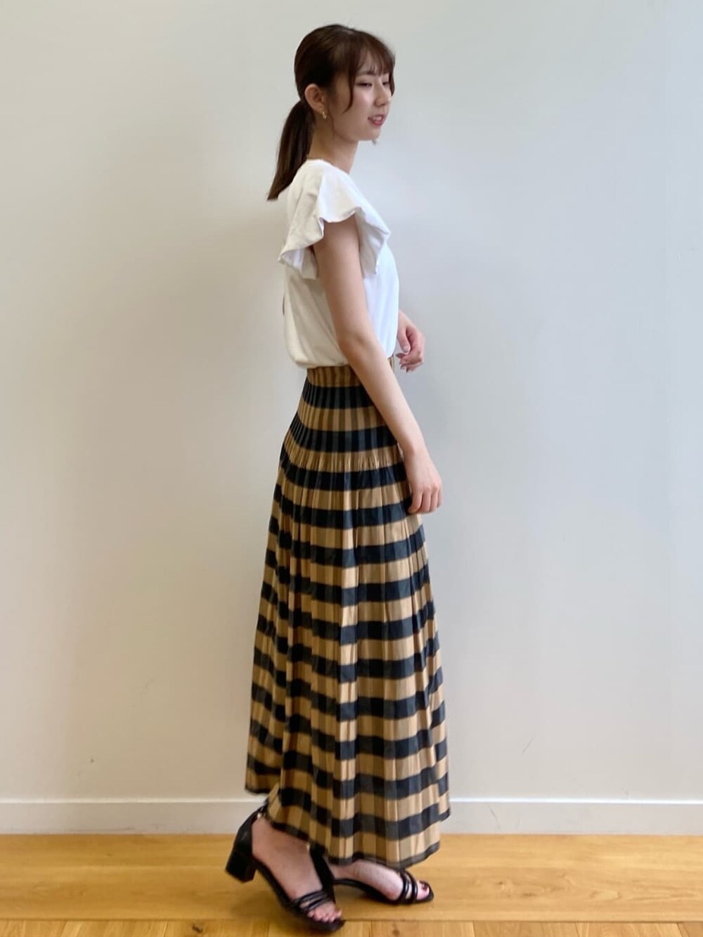 ベージュ系のスカート、ホワイト系のTシャツ/カットソー、ブラック系のサンダルを着用したレディースの夏コーディネートの3枚目の写真