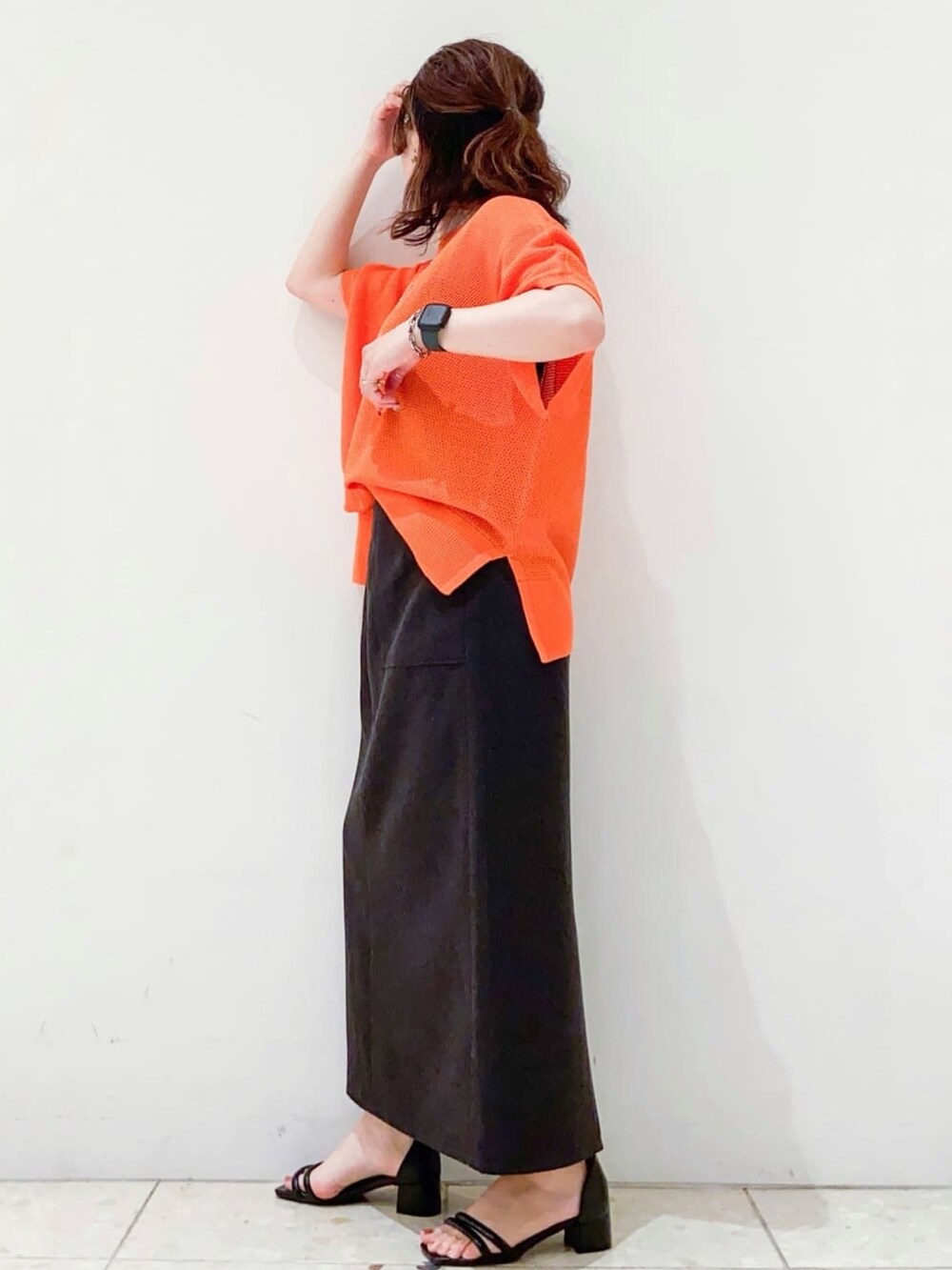 オレンジ系のニット/セーター、グレー系のスカート、ブラック系のショルダーバッグを着用したレディースの夏コーディネートの4枚目の写真