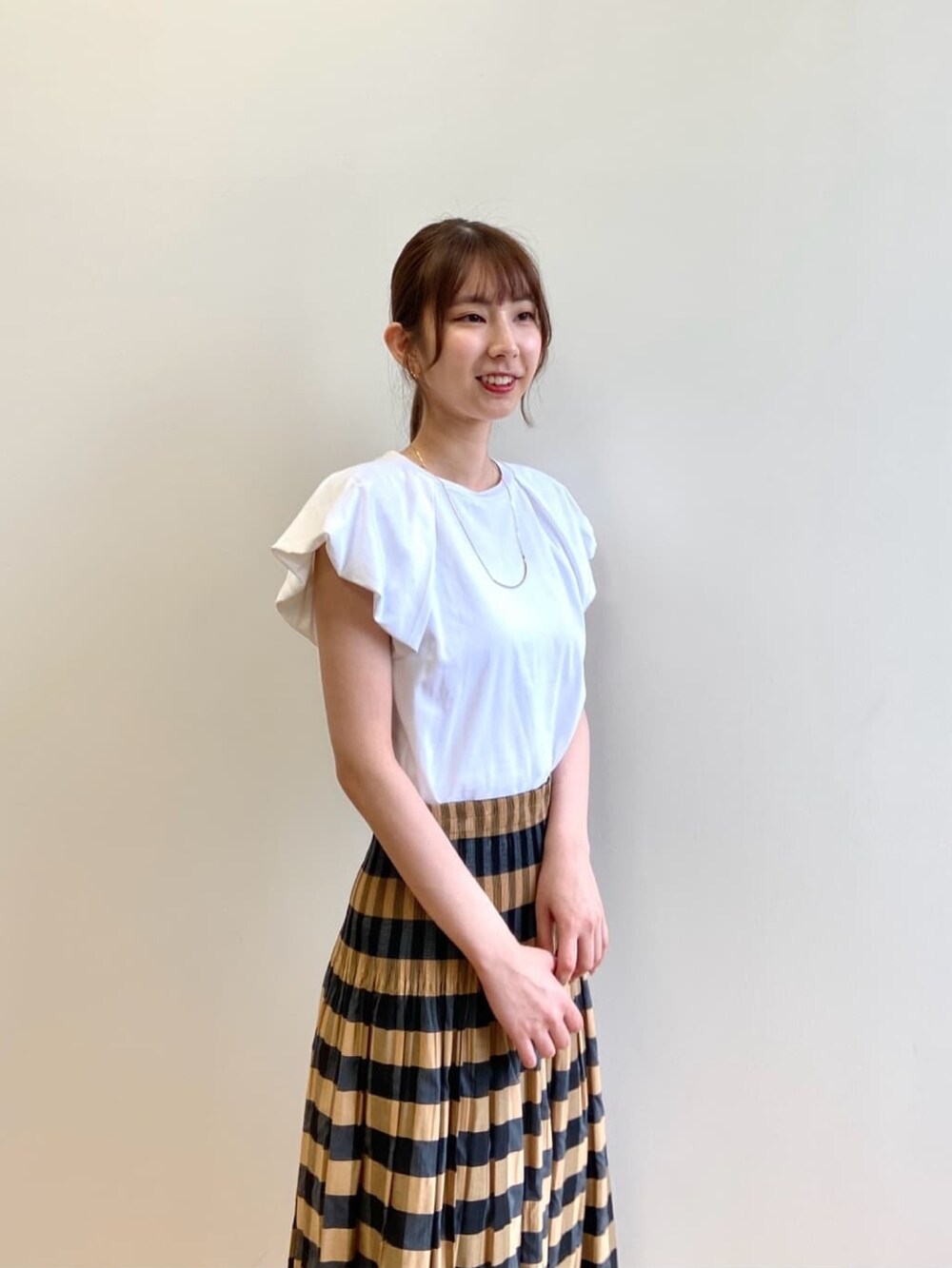 ベージュ系のスカート、ホワイト系のTシャツ/カットソー、ブラック系のサンダルを着用したレディースの夏コーディネートの7枚目の写真