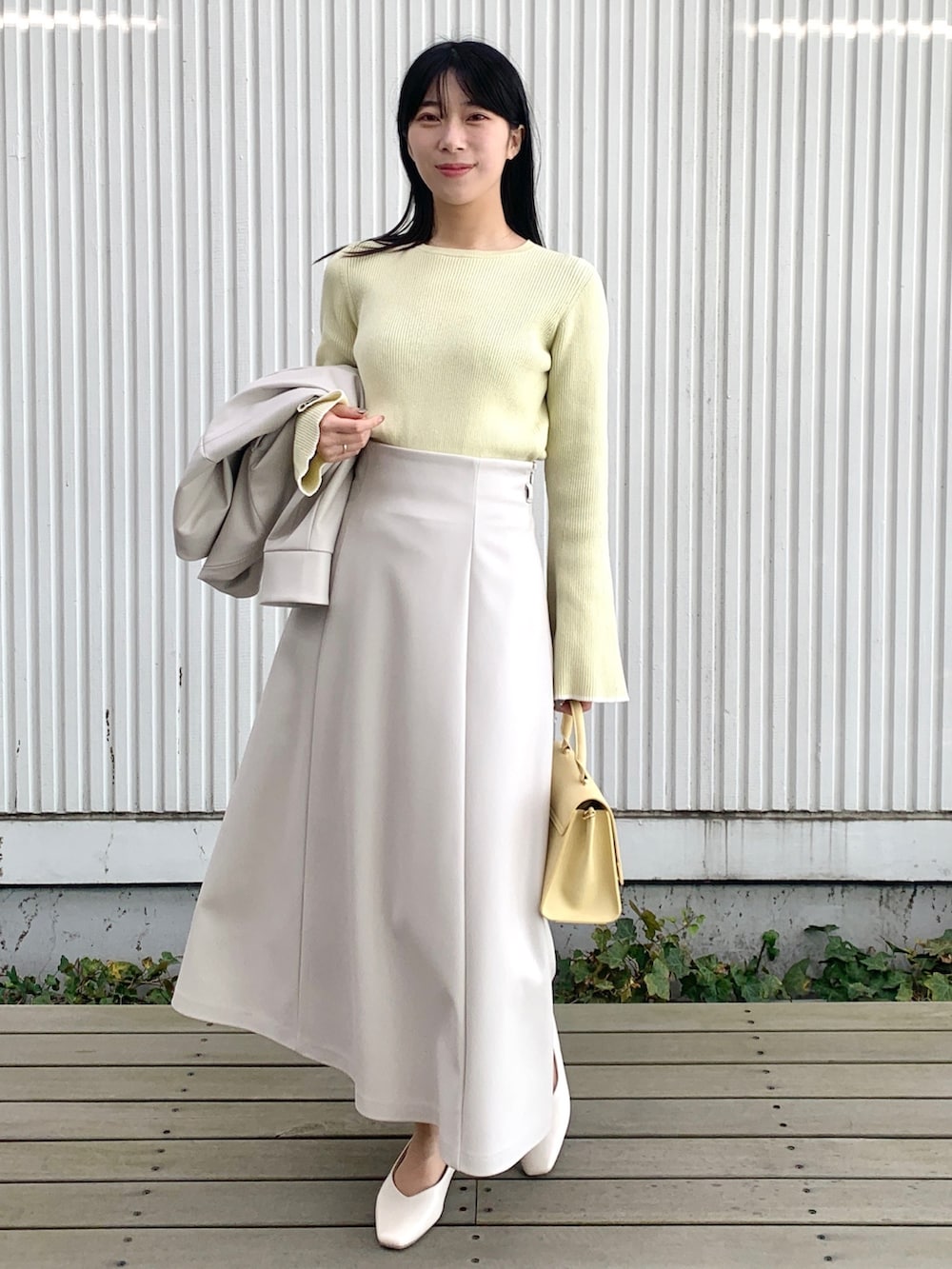 グレー系のブルゾン、イエロー系のニット/セーター、グレー系のスカートを着用したレディースの春コーディネートの2枚目の写真