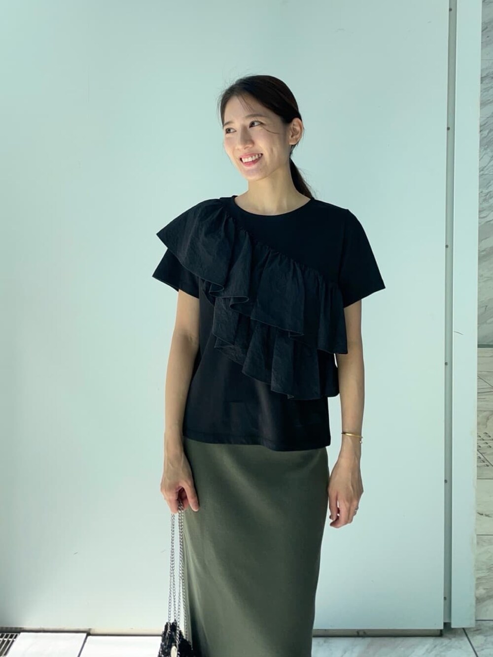 ブラック系のTシャツ/カットソー、グリーン系のスカート、シルバー系のパンプスを着用したレディースの夏コーディネートの2枚目の写真