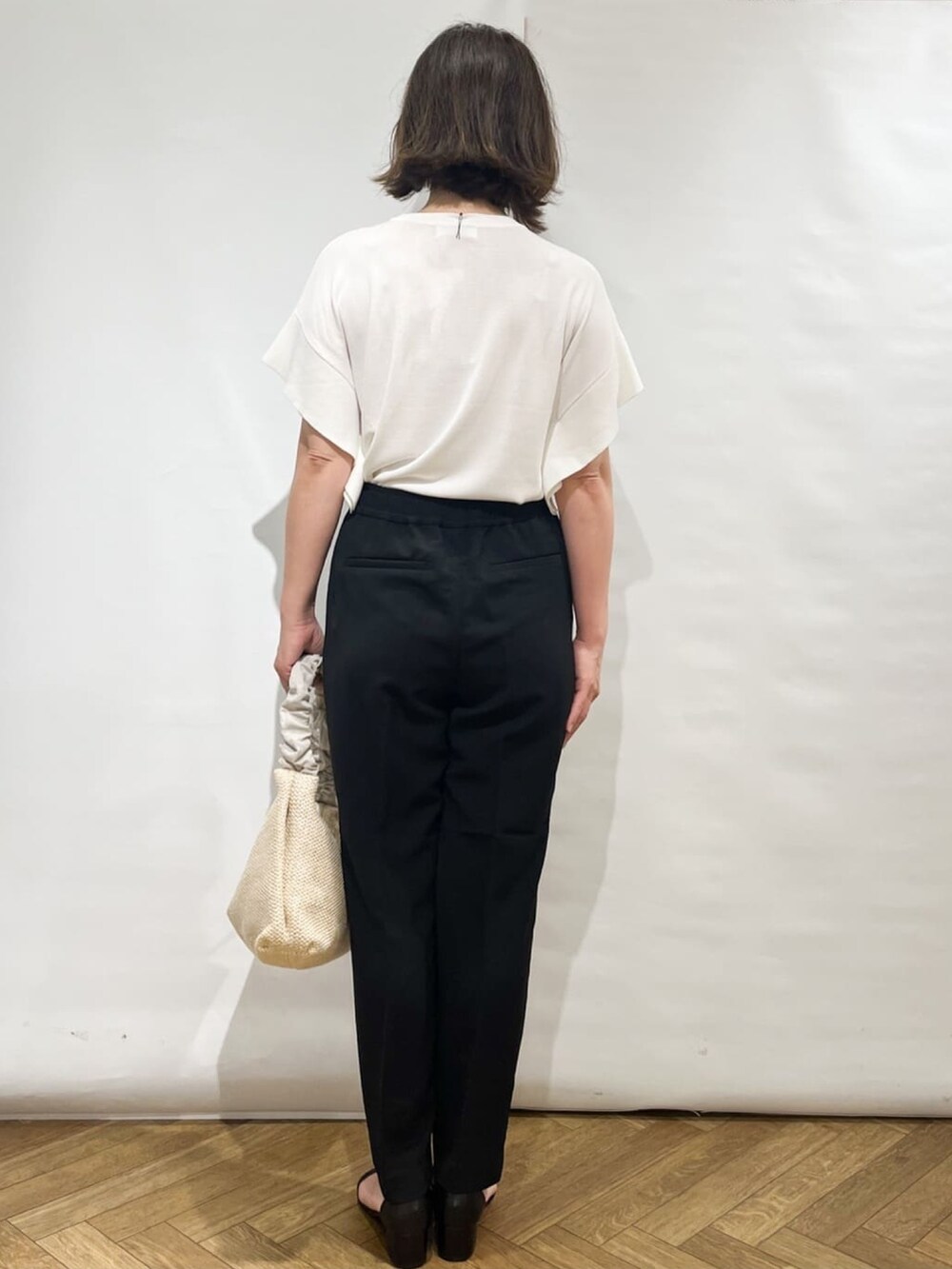 ホワイト系のニット/セーター、ブラック系のその他パンツ、ベージュ系のショルダーバッグを着用したレディースの夏コーディネートの4枚目の写真