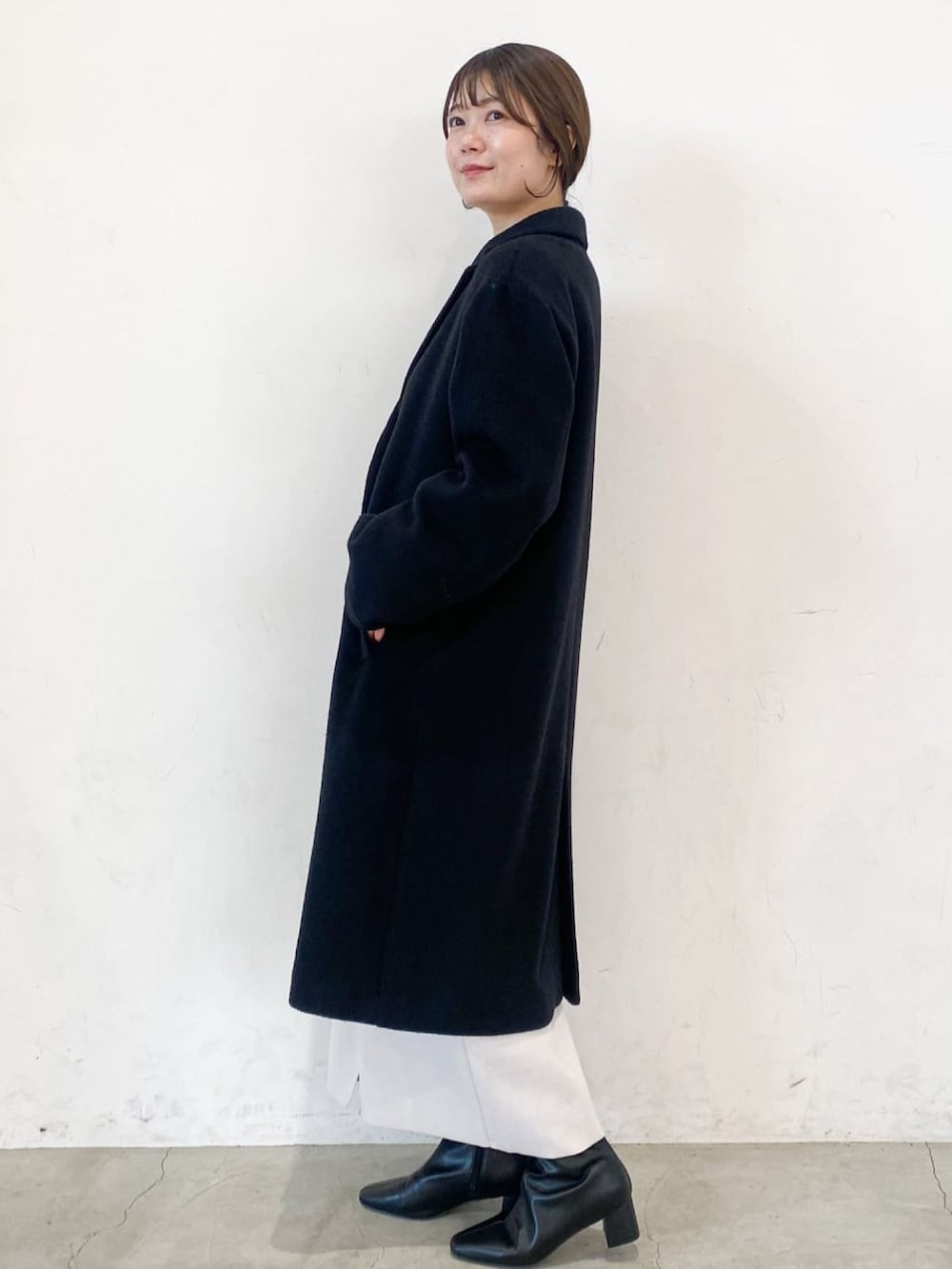 ブラック系のチェスターコート、オレンジ系のニット/セーター、ベージュ系のスカートを着用したレディースの冬コーディネートの3枚目の写真