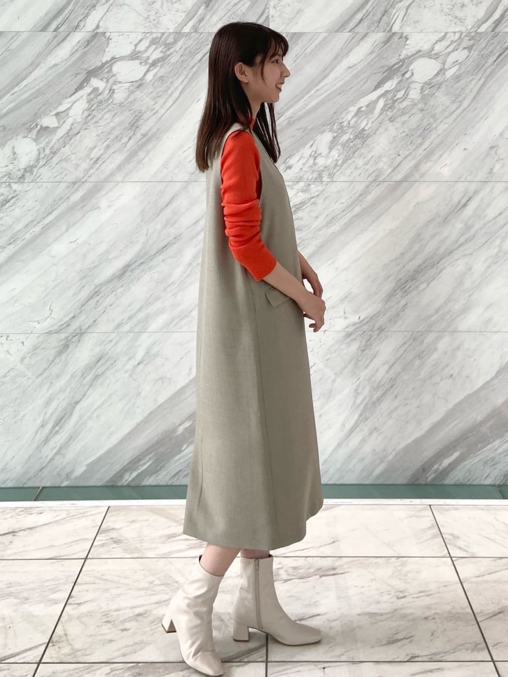 オレンジ系のニット/セーター、ベージュ系のワンピース、ホワイト系のブーツを着用したレディースの秋コーディネートの3枚目の写真