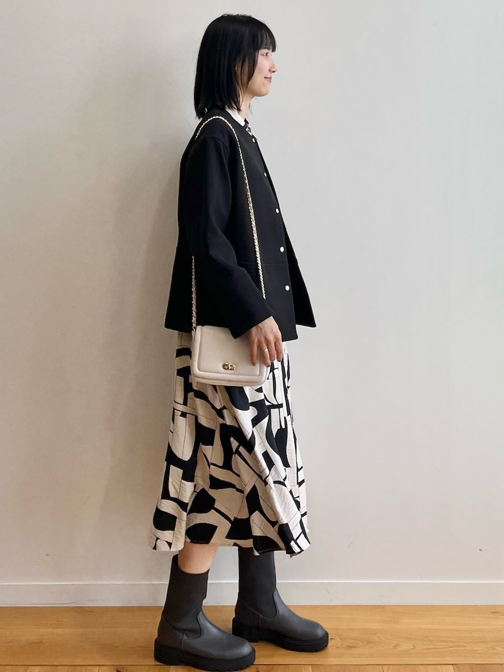 ブラック系のノーカラーコート、ベージュ系のワンピース、ブラック系のブーツを着用したレディースの秋コーディネートの2枚目の写真