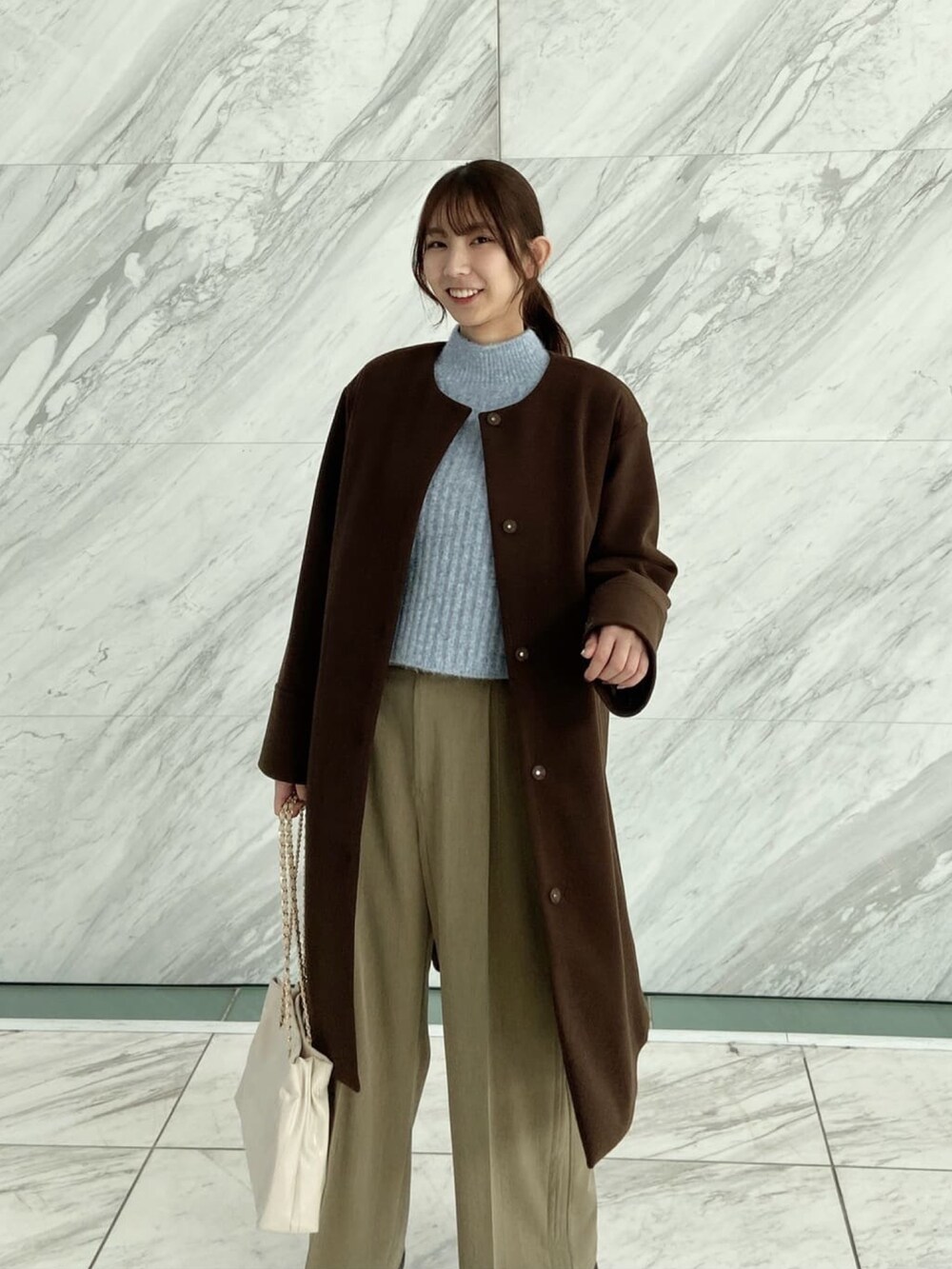 ブラウン系のノーカラーコート、ブラウン系のその他パンツ、ブルー系のニット/セーターを着用したレディースの秋コーディネートの5枚目の写真