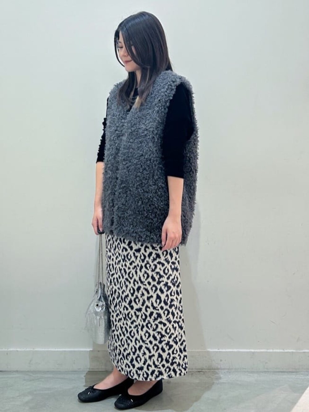 グレー系のベスト、ブルー系のスカート、ブラック系のTシャツ/カットソーを着用したレディースの秋コーディネートの2枚目の写真