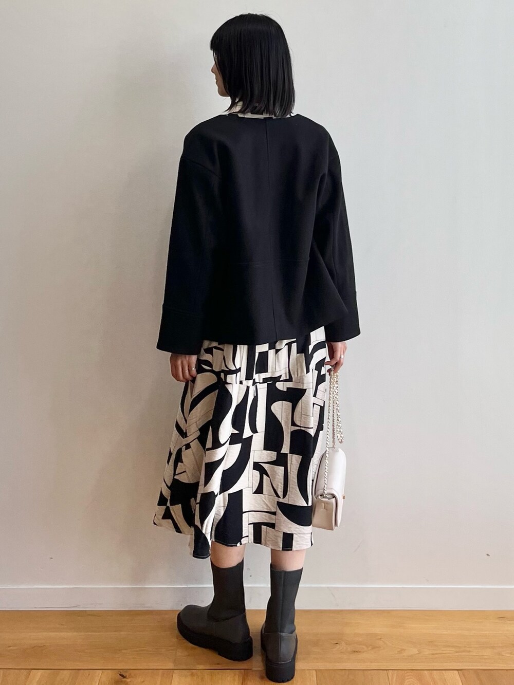 ブラック系のノーカラーコート、ベージュ系のワンピース、ブラック系のブーツを着用したレディースの秋コーディネートの3枚目の写真