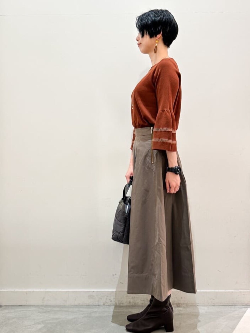 ブラウン系のスカート、グレー系のトートバッグ、ブラウン系のブーツを着用したレディースの秋コーディネートの2枚目の写真