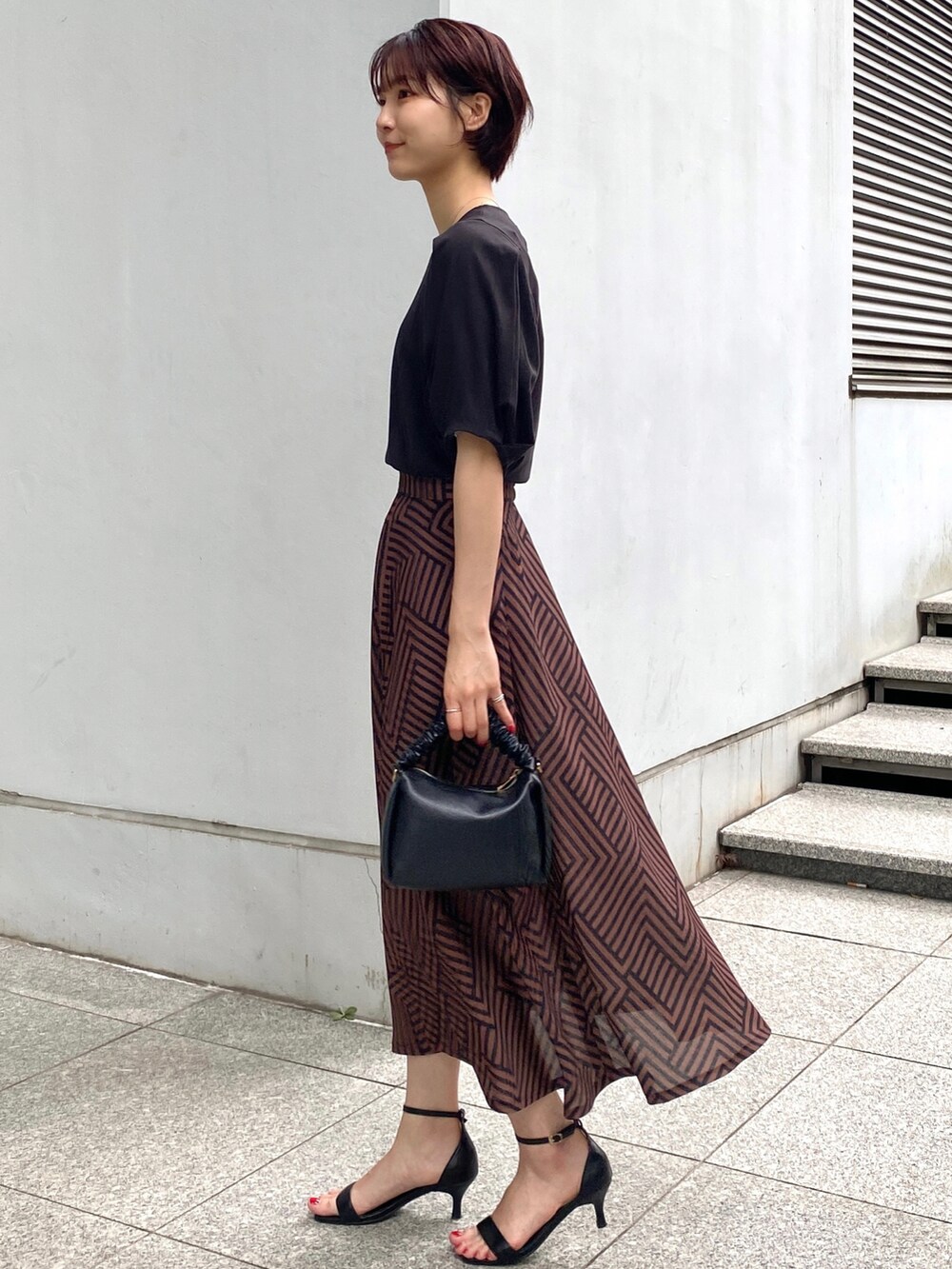 ブラウン系のスカート、ブラック系のTシャツ/カットソー、ブラック系のサンダルを着用したレディースの夏コーディネートの2枚目の写真