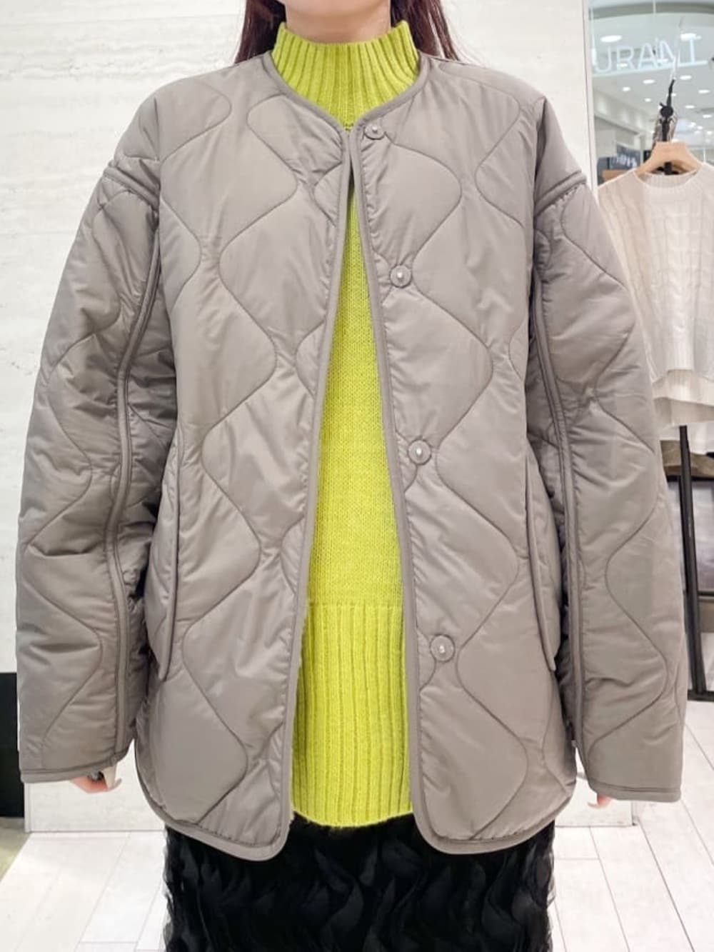 ブラウン系のノーカラーコート、イエロー系のニット/セーター、ブラック系のスカートを着用したレディースの冬コーディネートの3枚目の写真