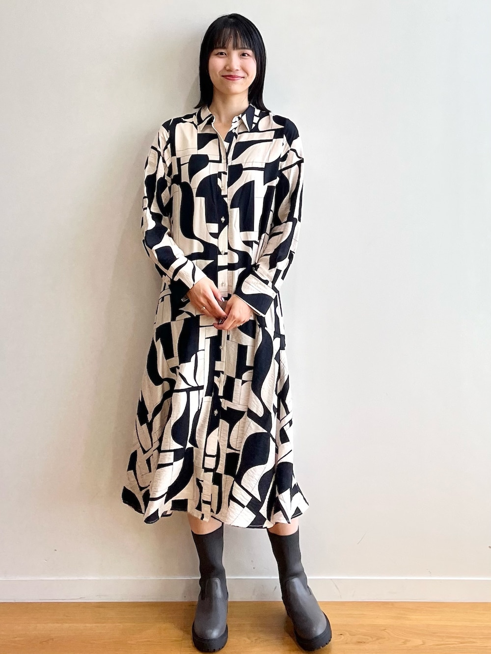 ブラック系のノーカラーコート、ベージュ系のワンピース、ブラック系のブーツを着用したレディースの秋コーディネートの7枚目の写真