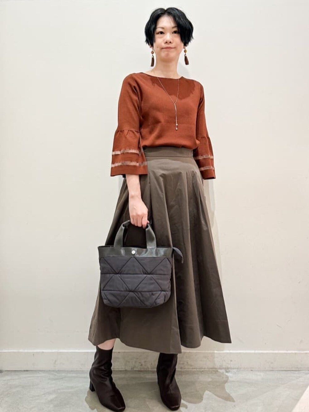 ブラウン系のスカート、グレー系のトートバッグ、ブラウン系のブーツを着用したレディースの秋コーディネートの4枚目の写真