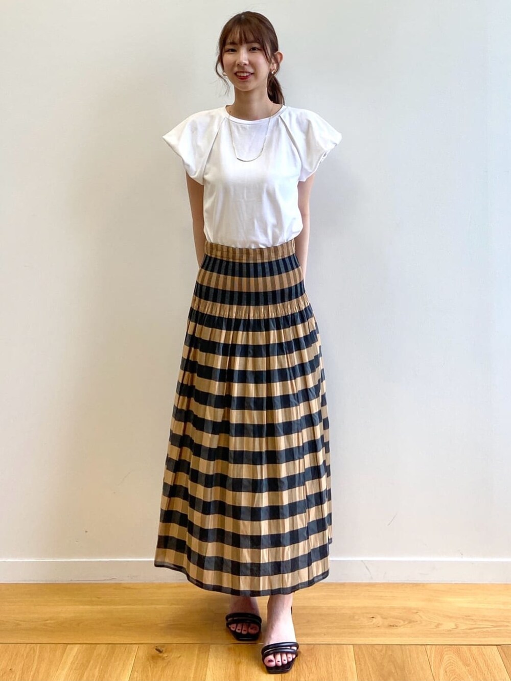 ベージュ系のスカート、ホワイト系のTシャツ/カットソー、ブラック系のサンダルを着用したレディースの夏コーディネートの2枚目の写真